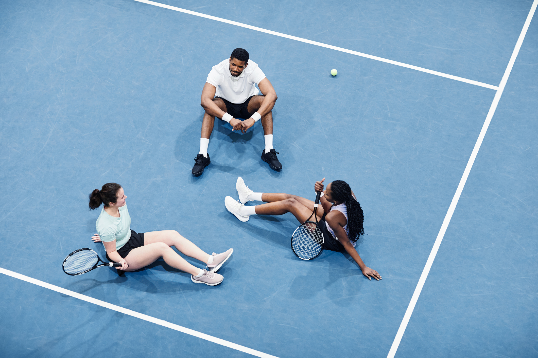 Minimal high angle at group of people relaxing at indoor tennis court and sitting on graphic blue flooring, copy space