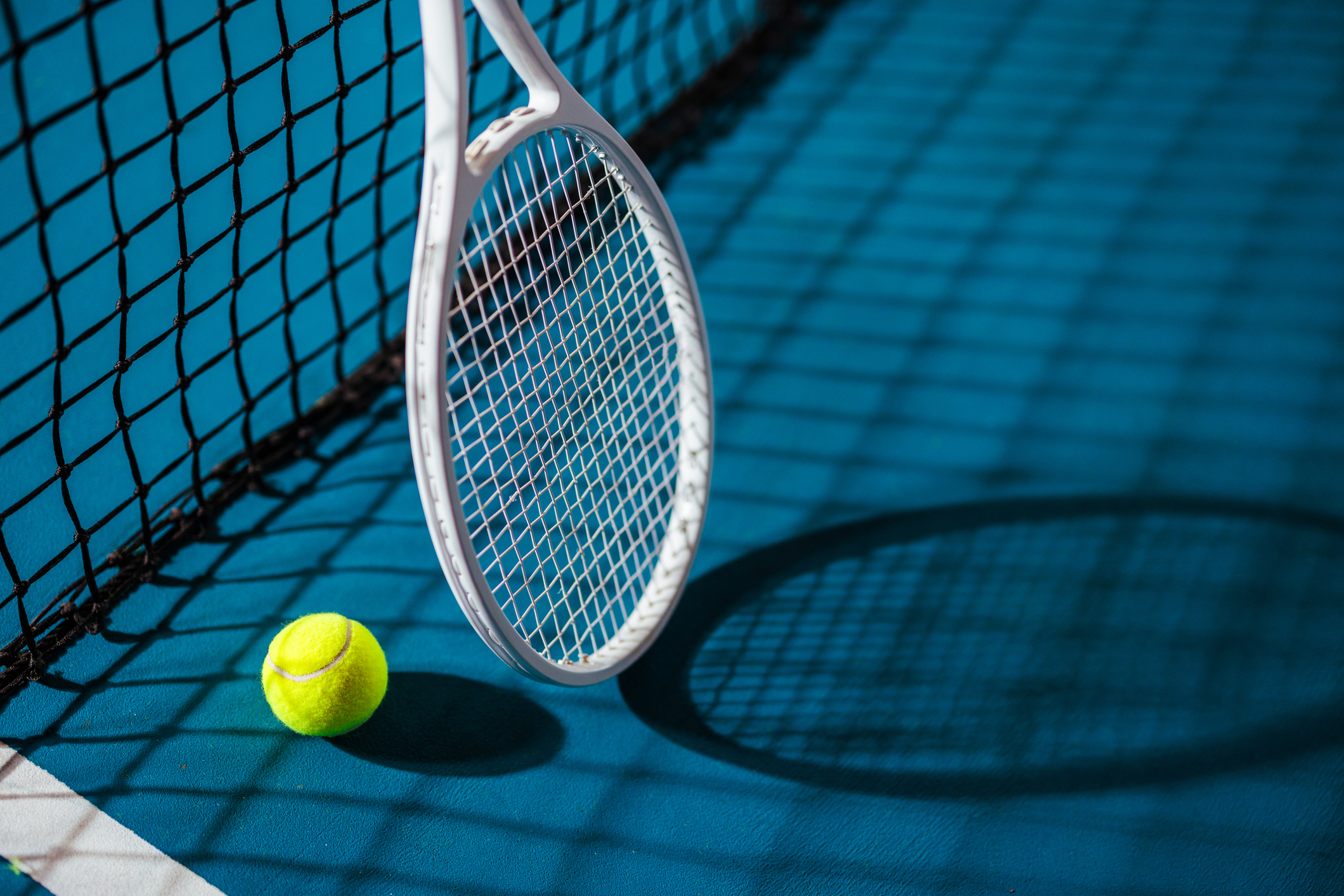 Close up of a white tennis racquet and a tennis ball by the net in bright atmospheric light with copy space.